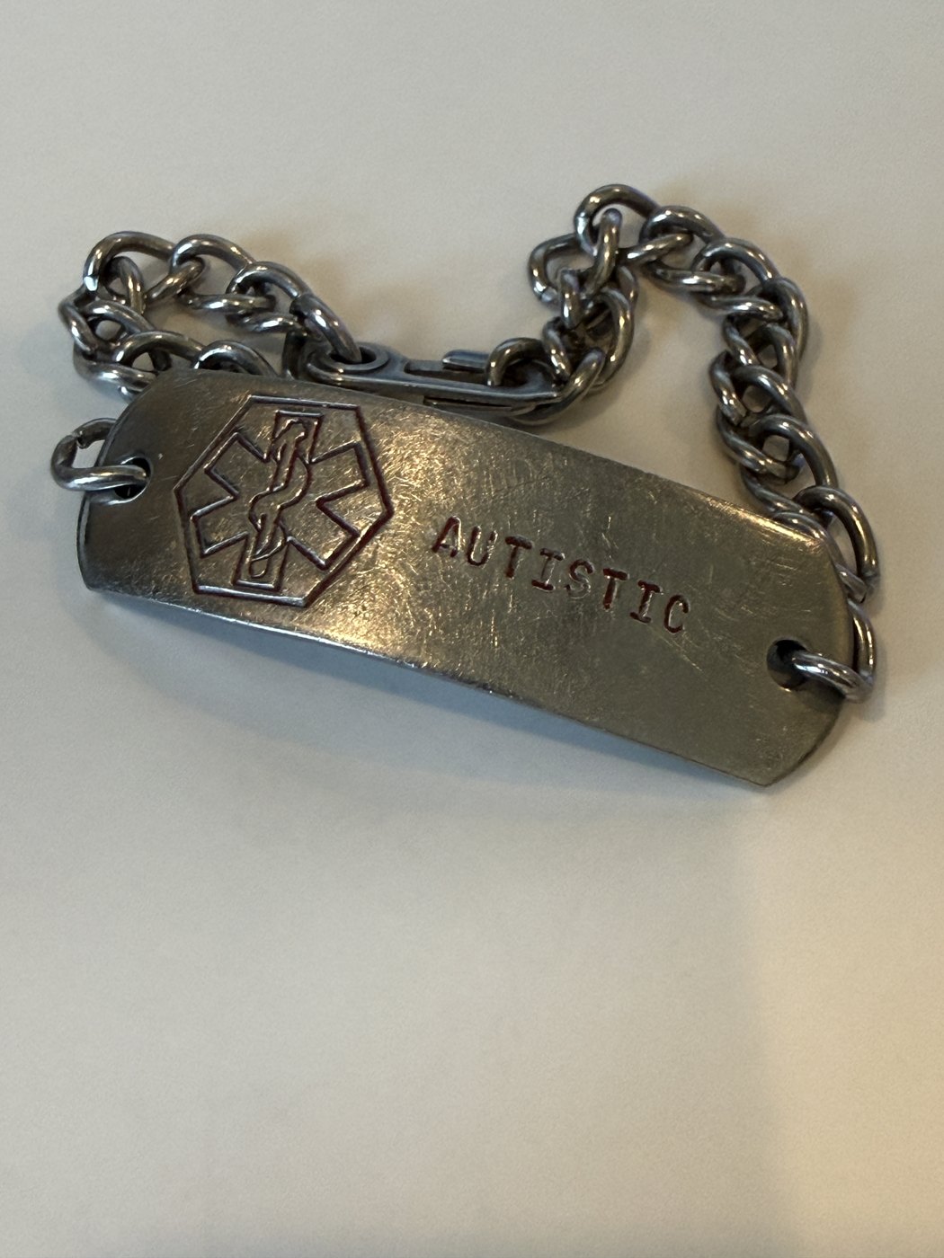 A stainless steel medical alert ID bracelet stamped AUTISTIC, with the medical alert star-of-life symbol